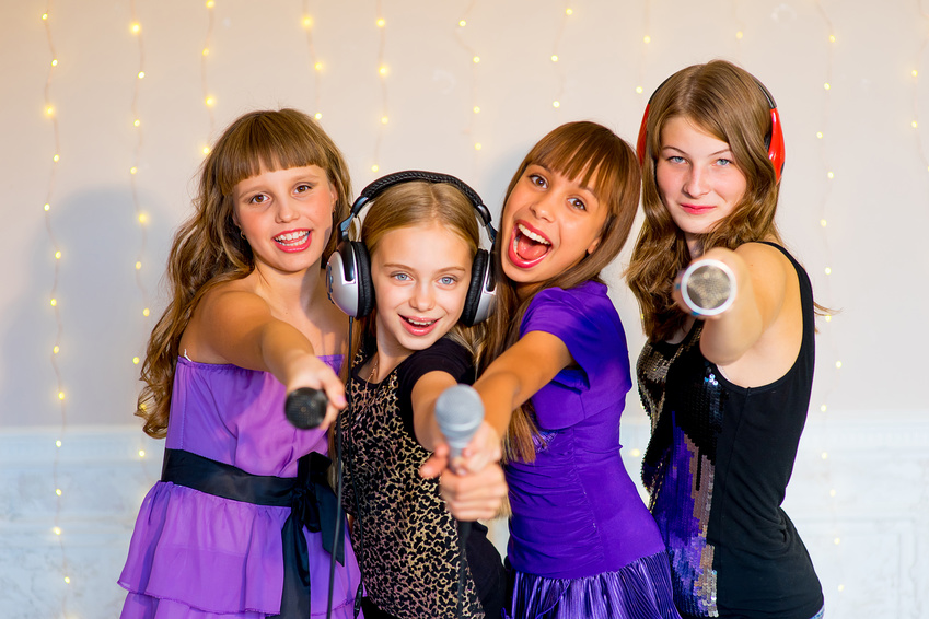 Group of happy girls with headphones singing together on karaoke on background of lights